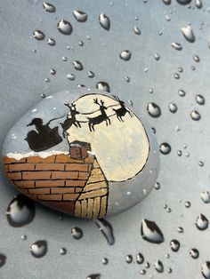 a rock painted with santa's sleigh and reindeers on top of a roof in the rain