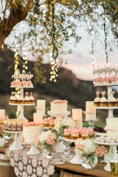 a table topped with lots of cakes and cupcakes next to a tree filled with flowers