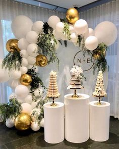 a table topped with white vases filled with cakes and desserts covered in gold and white balloons