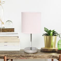 a pink lamp sitting on top of a wooden table next to a green potted plant