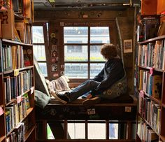 a person sitting on a window seat in a library filled with books and looking out the window