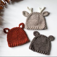 three crocheted hats sitting next to each other on a white surface with leaves