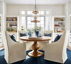 a dining room with chairs and a table in front of a large window that has built - in bookshelves