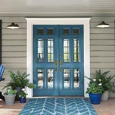 a blue front door with two potted plants on the side and an area rug