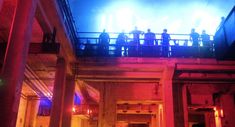 people are standing on the balcony of an old building with red, blue and yellow lights