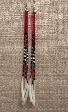 two red and black beaded earrings hanging from hooks on a beige wall with white fabric