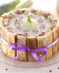 a close up of a cake on a glass plate with purple ribbon around it and vegetables in the background