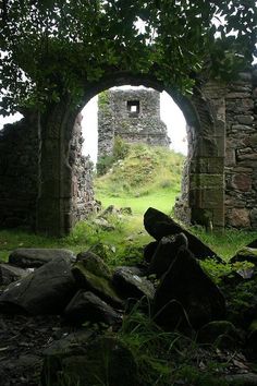 an arch in the side of a stone building with grass growing on it and rocks underneath