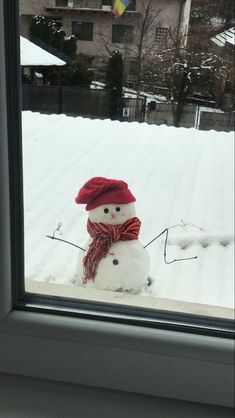 a snowman in a red hat and scarf is looking out the window at snowy yard