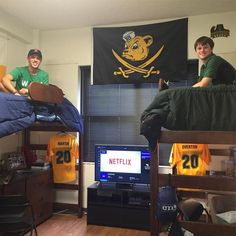 two boys are sitting on bunk beds in their dorm room, one is holding a football jersey