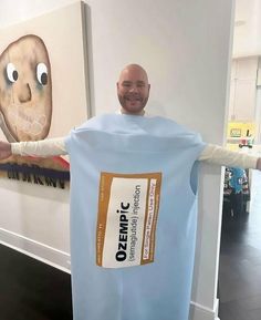 a bald man in a blue shirt is holding up a large bag that has been wrapped around his body