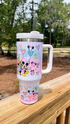 a travel mug with mickey and minnie mouses on it sitting on a wooden railing