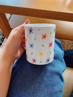 a woman is holding a coffee cup with flowers on the outside and inside, in front of a wooden table