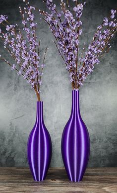 two purple vases sitting on top of a wooden table filled with lavender colored flowers