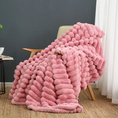 a large pink blanket sitting on top of a wooden chair next to a white table