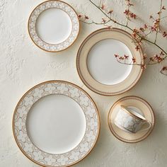 three plates and two cups on a table with flowers in vases next to them