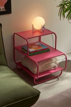 a pink table with some books on it next to a green couch and a plant