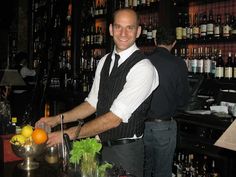 a man standing in front of a bar cutting an orange on top of a counter