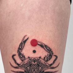 a black and white crab tattoo on the thigh, with a red dot in the center