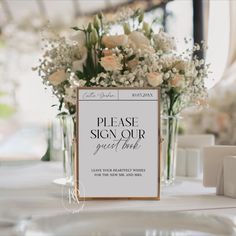 there is a sign that says please sign our guest book on the table with flowers in vases