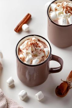 two mugs filled with hot chocolate and marshmallows on a white surface