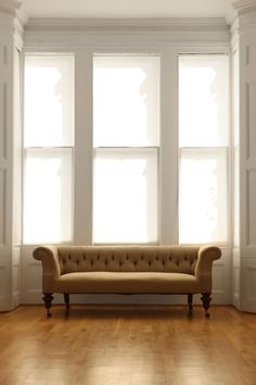 a couch sitting in front of three windows on top of a hard wood floor next to a wooden floor