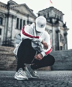 a man sitting on the ground in front of a building wearing a white and red hoodie