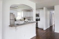 an empty kitchen with white cabinets and wood flooring is seen from the doorway to the living room