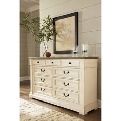 a white dresser with a mirror on top of it next to a rug and potted plant