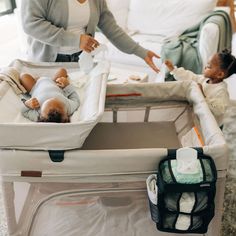 a woman standing next to a baby in a crib with another child laying on it