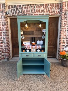 an old fashioned blue cabinet with coffee signs on the front and shelves below it, in front of a brick wall