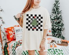 Checker Christmas Tree t-shirt.  These tees are Comfort Colors and are made to last using premium ringspun cotton, this creates an vintage-soft shirt. The soft-washed, garment-dyed fabric brings extra coziness to your wardrobe while the relaxed fit makes it an excellent daily choice. ✦ 100% Ringspun Cotton ✦ Relaxed fit ✦ Medium fabric ✦ Sewn-in twill label ✦ Eco-friendly, Ethically Made & Sweatshop Free ✦ Printed to order with non-toxic ink ✦ Durable and Long-lasting ✦ Shirts are pre-shrunk but may shrink slightly after washing ✦ Made to order: *Please allow 2-5 business days to print before being shipped* Sizing Recommendation: ✦ See size guide in images above ✦ This is a unisex t-shirt. Order your usual size for a relaxed fit, size down by one if you prefer a more fitted look, or size u Christmas Graphic Tee Shirt In Cotton, Christmas Cotton Graphic Tee Shirt, Tailgate Clothes, Funny Sports Shirts, Cherry Shirt, Retro Christmas Shirt, Color Checker, Xmas Tees, Christmas Retro