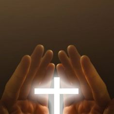 two hands holding a white cross in front of a dark background with the light shining through it