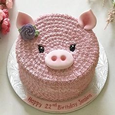 a pink birthday cake with a pig face on it's side and flowers in the background