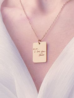 a woman wearing a white shirt and a gold necklace with a small square pendant that says, i love you again