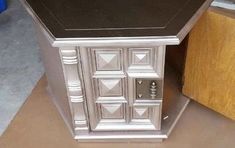 a silver and black cabinet sitting on top of a floor next to a wooden table