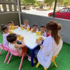 a group of children sitting around a white table with yellow cups in front of them