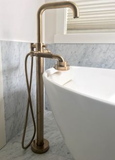 a white bath tub sitting under a window next to a sink with a faucet