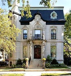 a large white house with black roof and two story front door, surrounded by trees