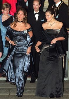 two women in evening gowns walking down the steps at an event with other people behind them