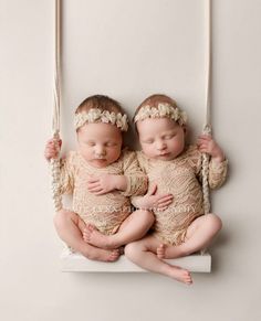 two baby babies are sitting on a swing with their arms around each other as if they were sleeping