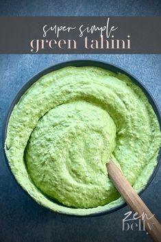 a bowl filled with green tahini next to a wooden spoon