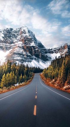 an empty road with mountains in the background and trees on both sides that are surrounded by snow