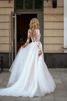 a woman in a white wedding dress is walking towards the door with her back to the camera