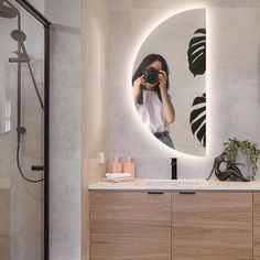 a woman taking a photo in front of a mirror on a bathroom counter with plants