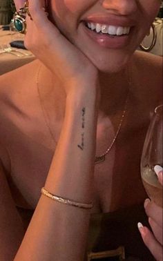 a woman with a tattoo on her arm holding a wine glass and smiling at the camera