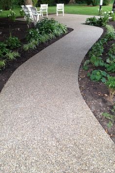 a walkway in the middle of a garden with chairs and trees around it, along with gravel