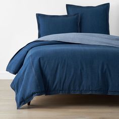 a bed with blue sheets and pillows on top of wooden floor next to white wall