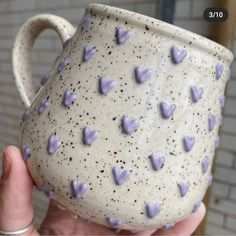 a hand holding a ceramic mug with purple hearts on the outside and white glaze