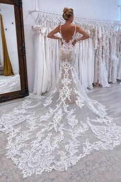 a woman standing in front of a mirror wearing a white wedding dress with an open back